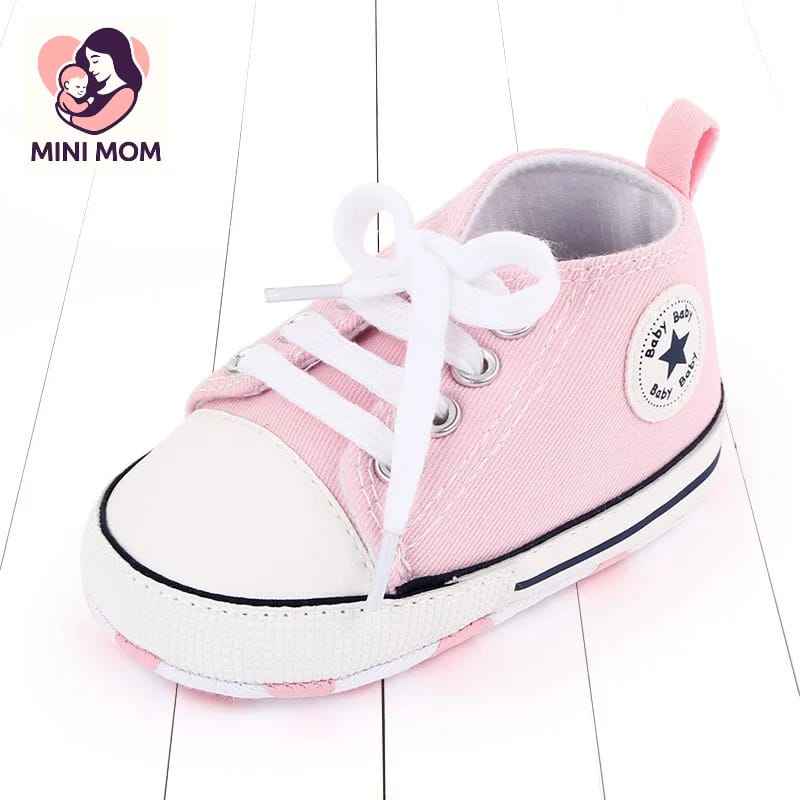Pink baby shoe with white laces on a light wooden floor, featuring the MINI MOM brand.