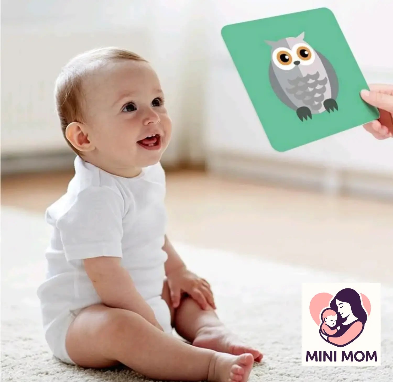 Baby sitting on a carpeted floor with a person holding a card with an owl illustration, and a Mini Mom logo in the corner.
