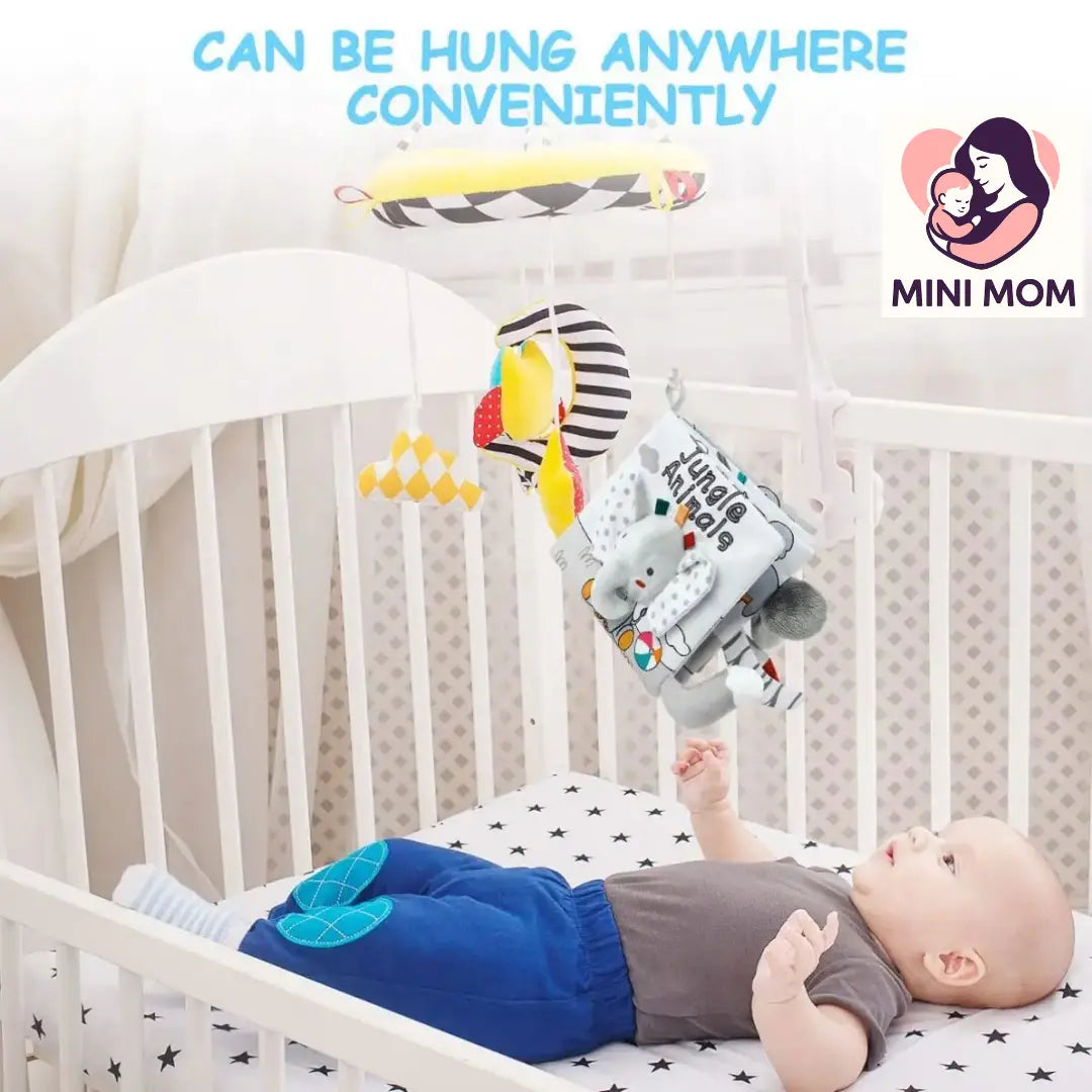 Baby lying in a crib with a colorful baby mobile above, featuring the brand 'Mini Mom'.