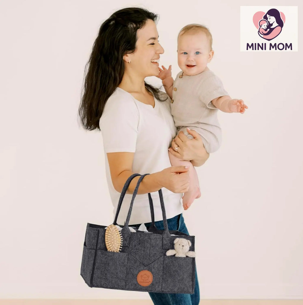 Woman holding a baby and a gray tote bag with a teddy bear, against a plain background with 'MINI MOM' logo.