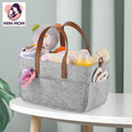 Gray diaper bag with brown handles filled with baby items on a white table, featuring the MINI MOM logo.