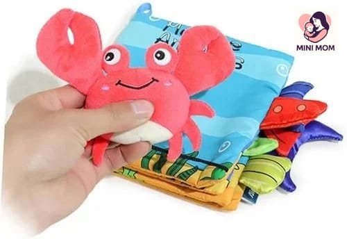 Colorful soft toy with a cartoon crab design held by a hand, branded 'MINI MOM'.