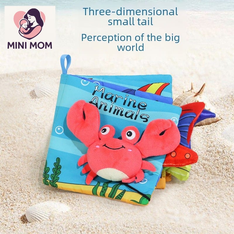 Children's soft book with a crab illustration on a sandy background, branded as MINI MOM.