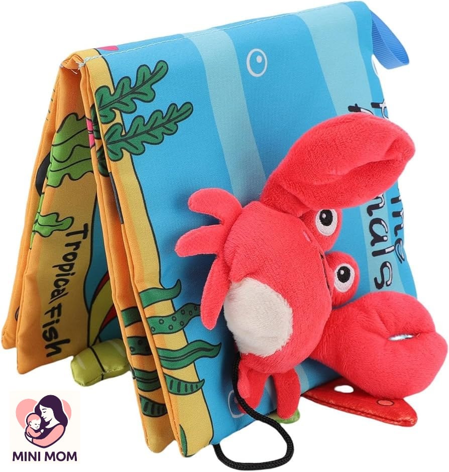Foldable baby cloth book with tropical fish design and red plush crab toy on a white background