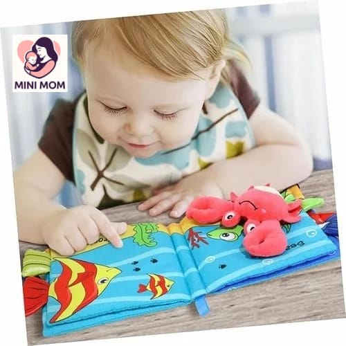 Child playing with a colorful soft book featuring sea creatures, with MINI MOM branding.